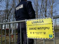 umundurowany policjant, za nim tabliczka informująca o covid-19