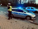 Umundurowany policjant z wydziału ruchu drogowego wykonuje pomiar prędkości.