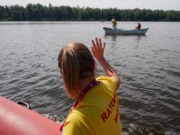 Kobieta macha rękom do mężczyzn na łódce.