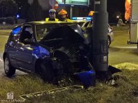 Na zdjęciu widoczny samochód który uderzył w słup trakcji trolejbusowej, a za nim strażacy i policjant.