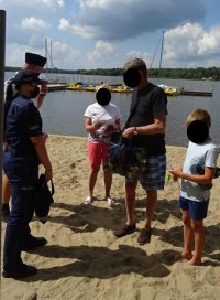 Policjanci podczas spotkania profilaktycznego rozmawiają z kobietą, mężczyzną i chłopcem o bezpieczeństwie nad wodą.