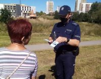 Dzielnicowy rozmawia z kobietą i podaje jej ulotki informacyjne dotyczące prowadzonych działań  pod nazwą &quot;Kręci mnie bezpieczeństwo nad wodą&quot;.