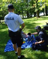 Policjanci rozmawiają o bezpieczeństwie z kobietą, która siedzi na kocu z małym dzieckiem.