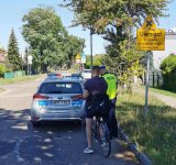 Policjant kontroluje rowerzystę podczas działań pod nazwą &quot;Bezpieczny rower&quot;. Przed nimi stoi radiowóz.