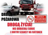 Na zdjęciu widoczny wóz strażacki pomiędzy dwoma samochodami oraz napis &quot;Droga pożarowa drogą życia!Nie odbieraj sobie i innym szansy na ratunek&quot; , &quot;Droga pożarowa-nie zastawiać.&quot;