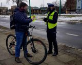 Policjantka rozmawia z rowerzystą i daje mu opaskę odblaskową.