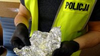 Policjant w odblaskowej kamizelce z napisem &quot;Policja&quot; trzyma folię aluminiową, w której znajduje się amfetamina.