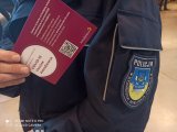 ramię umundurowanego policjanta, który w dłoni trzyma zaświadczenie o odbytym szczepieniu