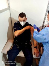 umundurowany funkcjonariusz siedzi na fotelu pielęgniarka podaje mu szczepionkę w ramie