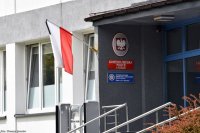 Biało-czerwona flaga z kirem oraz wejście do budynku Komendy Miejskiej Policji w Tychach.