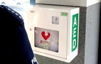 Na zdjęciu widoczny defibrylator AED oraz rękaw umundurowanego policjanta.