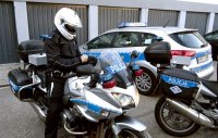 Dwa policyjne motocykle na jednym z nich siedzi policjant w kasku, w tle widoczny radiowóz.