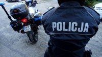 Napis &quot;Policja&quot; na mundurze policjanta, który stoi tyłem, przed nim policyjny motocykl.