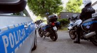 Dwa motocykle, na jednym siedzi policjant, widoczny bok radiowozu.