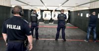 Na zdjęciu trzech umundurowanych policjantów jeden po cywilu, trzech funkcjonariuszy stoi na osi strzeleckiej z wyciągniętą bronią w stronę kulochwytu, za nimi stoi instruktor.