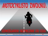 W górnej części plakatu znajduje się czerwony napis &quot;Motocyklisto zwolnij!&quot;. Na środku plakatu jest droga, a na niej motocyklista. W dolnej części plakatu znajduje się czerwony napis &quot;Jednośladem bezpiecznie do celu&quot;.