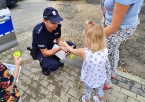 Umundurowany policjant daje dziewczynce odblask.