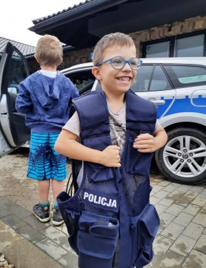 Uśmiechnięty chłopiec ma założona policyjna kamizelkę.