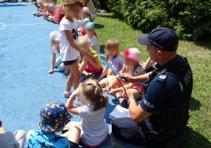 Policjant daje dziewczynce opaskę odblaskową, widoczne inne dzieci.
