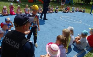 Policjant przekazuje chłopcu opaskę odblaskową, widoczne inne dzieci.