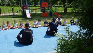 Dzieci siedzą na niewielkim boisku na przeciwko dwóch policjantów i rozmawiają o bezpieczeństwie.