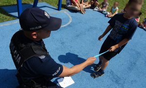 Policjant przekazuje chłopczykowi opaskę odblaskową.