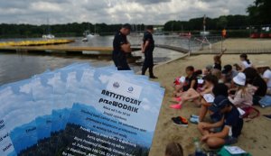 Ulotki: Artystyczny Przewodnik&amp;quot; w tle policjanci i dzieci na plaży.