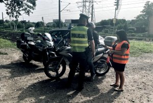 Pani z Polskich Linii Kolejowych, umundurowany policjant rozmawiają z motocyklistą, w tle widoczny radiowóz.