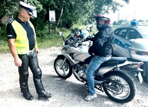 Umundurowany policjant stoi obok motocyklisty, który siedzi na policyjnym motocyklu.