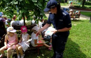 Policjantka podaje dziewczynce kolorowankę. Obok siedzą inne dzieci.