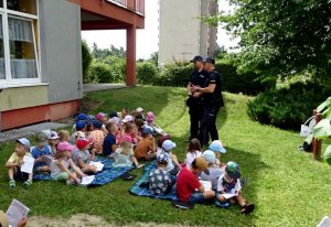 Policjanci rozmawiają z dziećmi, które siedzą na kocach.