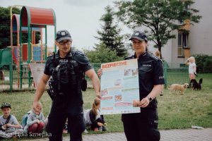 Policjant i policjantka trzymają plakat dotyczący bezpiecznych wakacji.