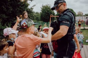 Chłopiec ogląda umundurowanie policjanta, w tle widoczne inne dzieci.