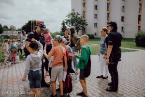 Policjant rozmawia z grupą dzieci, obok stoi policjantka oraz kobiety.