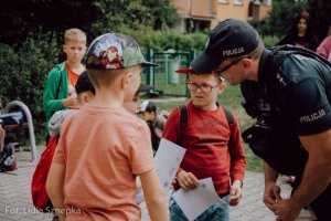 Policjant pochyla się do dzieci, z którymi rozmawia.