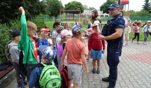 Policjant rozmawia z dziećmi, które przed nim stoją.