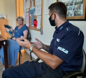 umundurowany policjant rozmawia z seniorką. oboje siedzą na krzesłach.