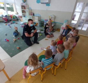 Dzieci siedzą na przeciwko policjanta, który z nimi rozmawia.