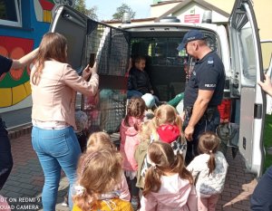 Policjant stoi przy radiowozie, w środku oraz obok pojazdu są dzieci, kobieta robi zdjęcia.