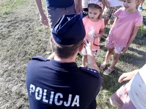 Umundurowany policjant kuca przy dziewczynce obok stoi kolejna dziewczynka.