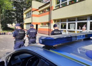 Umundurowani policjanci, stoją przodem do dzieci,widoczny radiowóz.