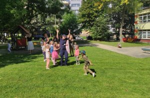 Na trawie przed przedszkolem widoczne dzieci i policjantka.