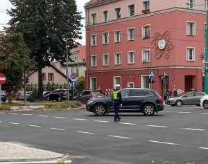 Umundurowany policjant wydziału ruchu drogowego stoi na skrzyżowaniu i kieruje ruchem.