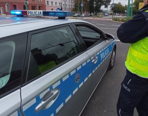 Widoczny radiowóz na środku skrzyżowania oraz część munduru policjanta .