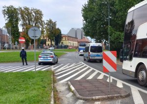 Radiowóz pilotuje autokar, obok inny radiowóz i policjant.