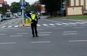 Policjant w żółtej kamizelce na skrzyżowaniu kieruje ruchem.