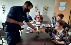 Policjant zakłada opaskę odblaskową seniorce, widoczne inne kobiety.