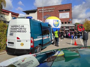 Przed budynkiem Wojewódzkiego Ośrodka Ruchu Drogowego stoi radiowóz inspekcji Transportu Drogowego, wóz Straży Pożarnej, obok stoją osoby.