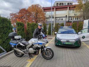 Policjant wydziału ruchu drogowego obok motocykl i radiowóz inspekcji transportu drogowego.