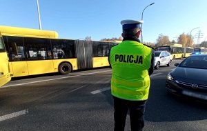 Policjant w żółtej kamizelce z napisem &quot;Policja&quot; stoi przed autobusem komunikacji miejskiej.